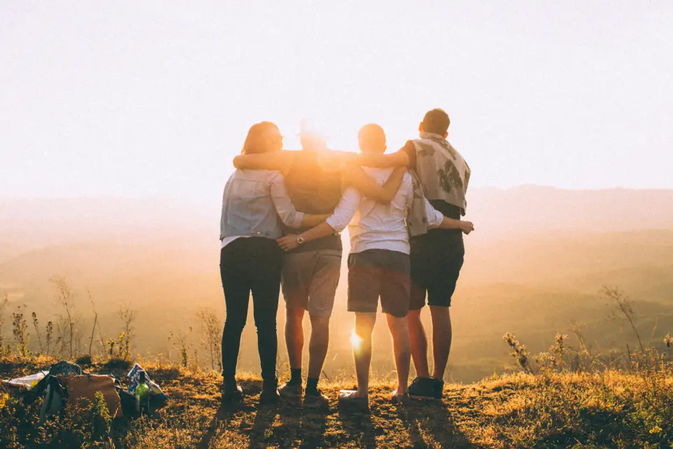 Des amis bras dessus bras dessous, face au soleil couchant sur les montagnes
